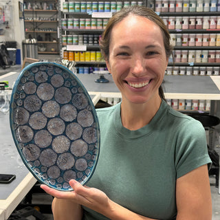 A member holding an oval platter with a teal rim and a pattern of gray round cells at The Clay Hole pottery studio in Draper, Utah
