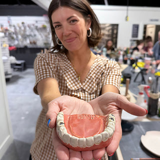 A member holding out a piece shaped like a set of teeth, with white teeth and a pink gum base at The Clay Hole pottery studio in Draper, Utah
