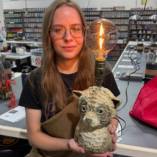 A member holding a textured gray and tan animal head with a lit light bulb on top at The Clay Hole pottery studio in Draper, Utah