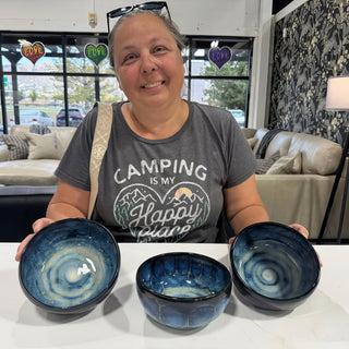 A member sitting behind three glossy bowls with deep blue swirling glaze on the insides at The Clay Hole pottery studio in Draper, Utah