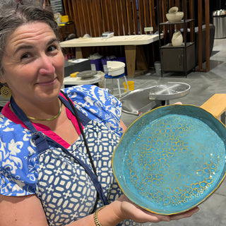 A member holding a round turquoise platter with a lacy crackled pattern inside and a gold colored rim at The Clay Hole pottery studio in Draper, Utah