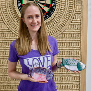 A member holding two fish-shaped dishes, one pink and purple with blue dots and one teal and white at The Clay Hole pottery studio in Draper, Utah
