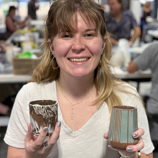 A member holding two cups, one streaked white and brown and one with vertical teal stripes at The Clay Hole pottery studio in Draper, Utah