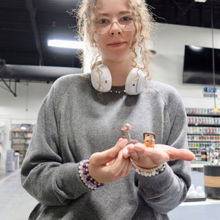 A member holding out two tiny figures in an open hand, one gray and one orange at The Clay Hole pottery studio in Draper, Utah
