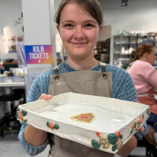 A member holding a shallow white square dish with raised red and green flowers on the sides at The Clay Hole pottery studio in Draper, Utah