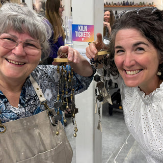 Two members holding up wind chimes strung with dark star-shaped pieces, gold beads and long thin strips at The Clay Hole pottery studio in Draper, Utah