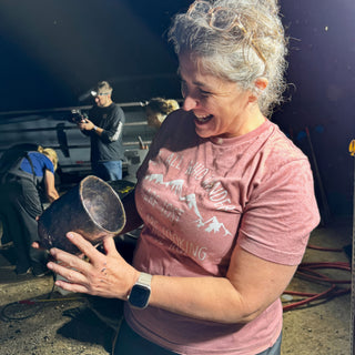 A laughing person in a pink shirt tilts a dark glossy vessel with a speckled surface toward the camera at The Clay Hole in Draper, Utah