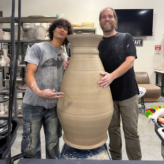 Two friends pose with their arms around a huge tan vase with faint horizontal ridges at The Clay Hole in Draper, Utah