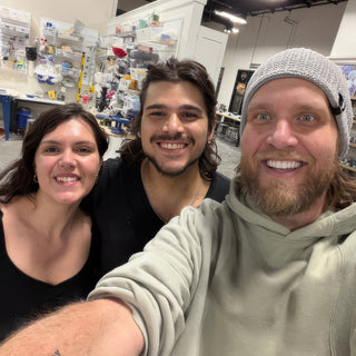 Three smiling people crowd into a selfie inside a pottery studio, with shelves of supplies on the wall behind them at The Clay Hole in Draper, Utah