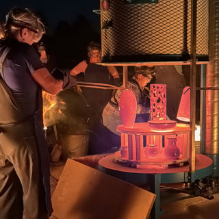 Potters with tongs gather at a kiln where glowing orange vases, a pierced cylinder and a bowl sit at The Clay Hole in Draper, Utah