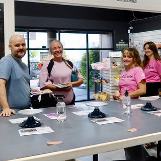 Four smiling people stand and sit at a long gray table with turntables and handouts, two wearing pink shirts at The Clay Hole in Draper, Utah