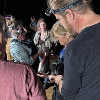A crowd in headlamps gathers around a tall ridged vase with a coppery finish held by one person at The Clay Hole in Draper, Utah
