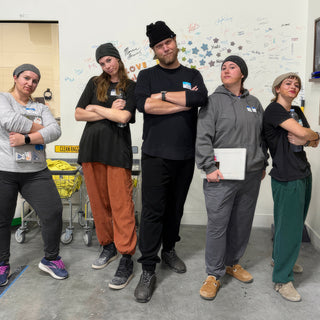 Five people in knit beanies posing with arms crossed and heads tilted in front of the signature wall at The Clay Hole in Draper, Utah