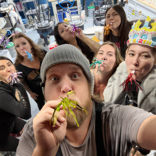 A group crowds into a selfie blowing party horns while one wears a birthday crown at The Clay Hole in Draper, Utah