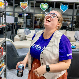 A person laughing with head tipped back in a purple t-shirt and striped vest, holding a can at The Clay Hole in Draper, Utah