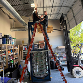 Two people work from an orange ladder on a large blue metal frame beside a forklift at The Clay Hole in Draper, Utah