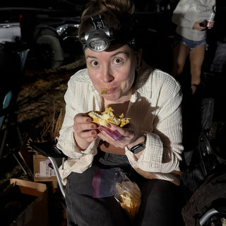 A potter in a headlamp and cream shirt takes a bite of a sandwich, with chips in their lap at The Clay Hole in Draper, Utah