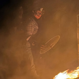 A potter in goggles and a plaid shirt holds a round metal lid in thick orange smoke at The Clay Hole in Draper, Utah