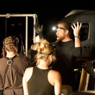A potter in a headlamp raises one hand while talking to a group beside a metal frame at The Clay Hole in Draper, Utah