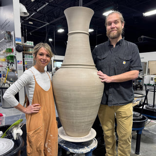Two potters stand beside a vase taller than they are, with a flared rim and a ring at the neck at The Clay Hole in Draper, Utah