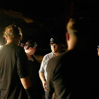 A group of potters in headlamps stand close together in the dark and look off to one side at The Clay Hole in Draper, Utah