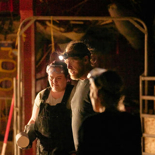 Three potters in headlamps stand close together near a metal frame, one holding a small plain white cylinder at The Clay Hole in Draper, Utah