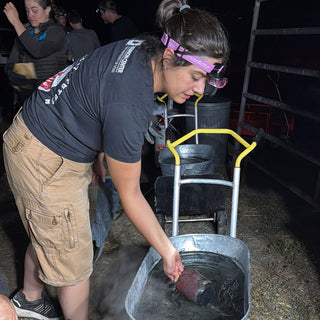 A person in a headlamp leans over a metal tub and reaches toward a reddish brown pot in steaming water at The Clay Hole in Draper, Utah