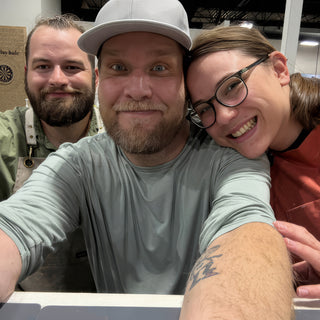 Three people lean together for a close selfie, the middle one in a gray cap and green shirt at The Clay Hole in Draper, Utah
