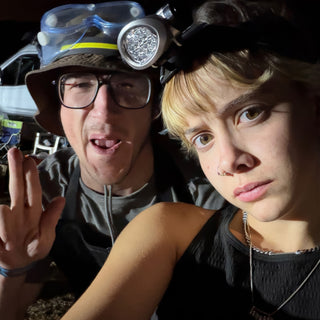 Two friends crowd into a close selfie at night, one wearing a bucket hat with goggles and a headlamp at The Clay Hole in Draper, Utah