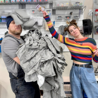 Two people joke around in front of a supply wall, one holding a big pile of gray fabric at The Clay Hole in Draper, Utah