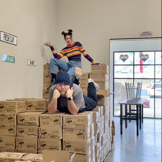 Two potters pose on stacked cardboard boxes, one lying with chin in hands and one perched above at The Clay Hole in Draper, Utah