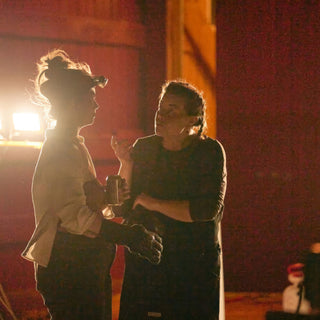 Two potters in headlamps and aprons talk in warm orange light, one holding a small metal cup at The Clay Hole in Draper, Utah
