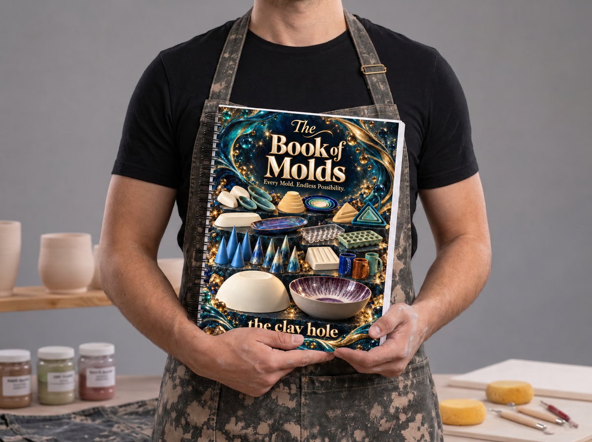 A potter in a clay splattered apron holding the spiral bound, printed Book of Molds from The Clay Hole