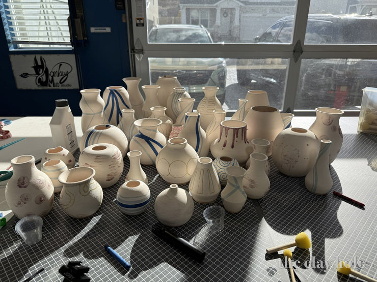 Bud vases painted with underglaze designs drying on a table by a garage door window