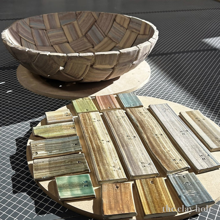 Basketweave bowl woven from marbled clay strips next to numbered glaze test tiles in sunlight